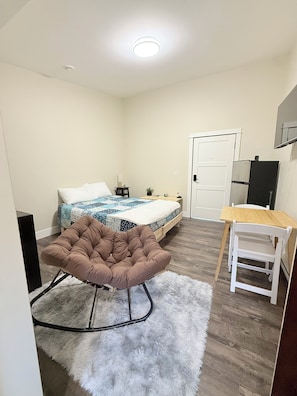 A bedroom with a bed, a chair, a desk, and a door.