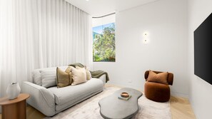 Ein modernes Wohnzimmer mit einem grauen Sofa, einem braunen Sessel, einem Couchtisch und einem Fenster mit Blick auf Grünflächen.