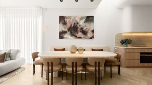 Ein stilvoller Essbereich mit rundem Tisch, sechs Stühlen, einer Couch und einem großen, abstrakten Gemälde an der Wand.