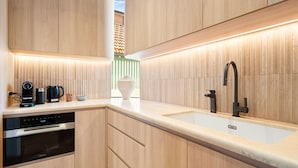 A modern kitchen with wooden cabinetry, a stainless steel dishwasher, a black coffee maker, and a sleek faucet. - Sol Coastal Luxury in Bondi Beach (Bondi Beach)