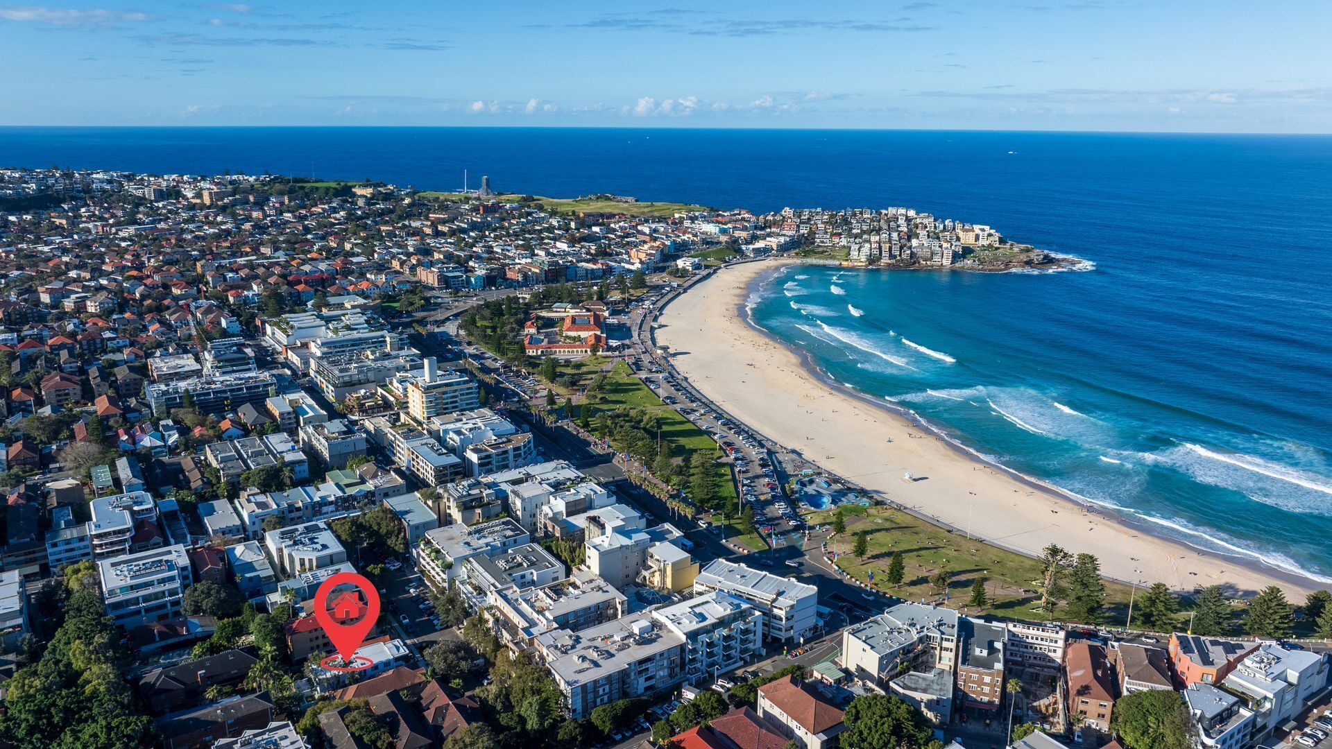 An aerial view of a coastal city with a beach, residential buildings, and a marked location.