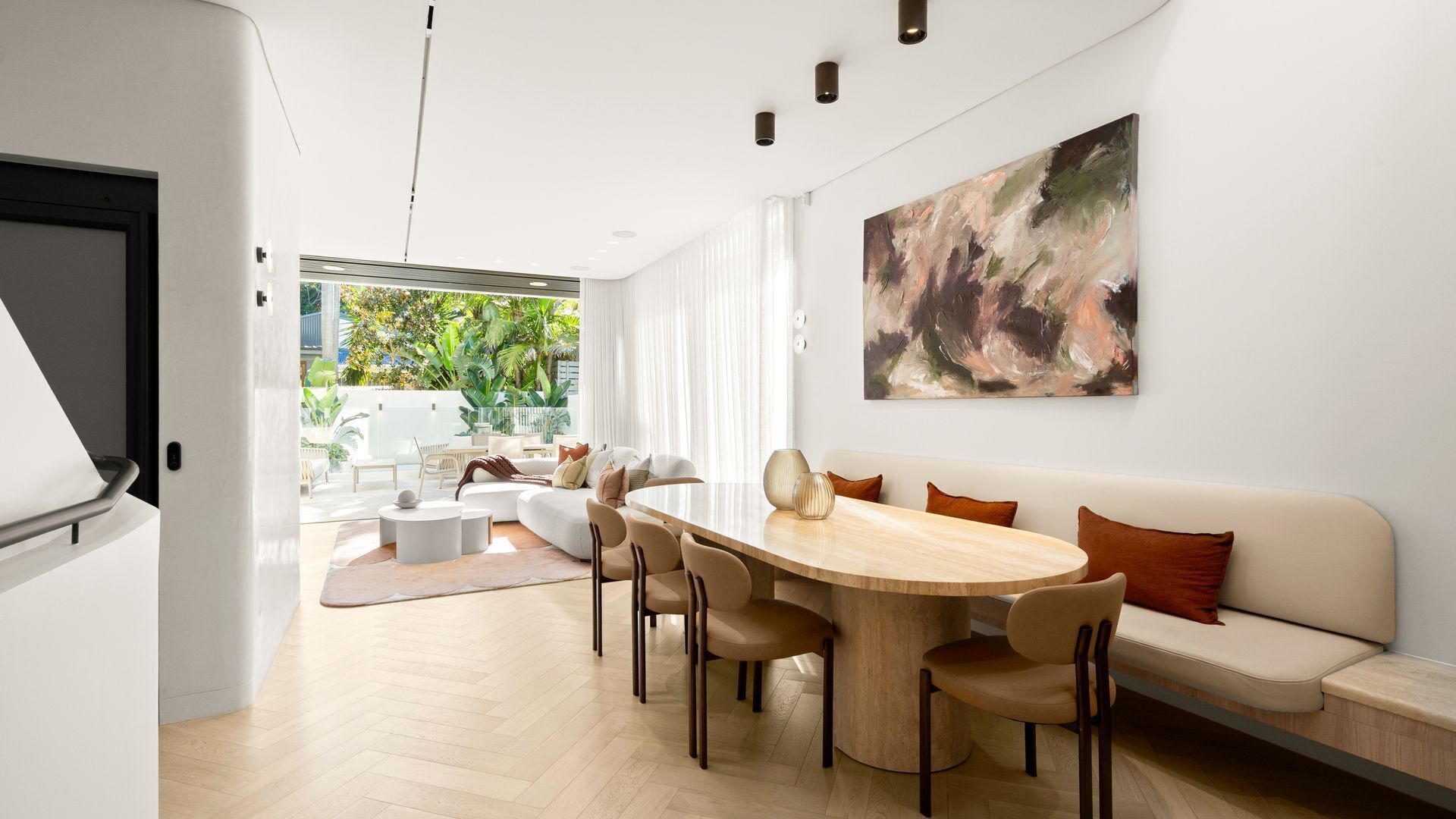 Un salon moderne comprenant un coin repas, une grande peinture abstraite et une vue sur la verdure à l’extérieur.