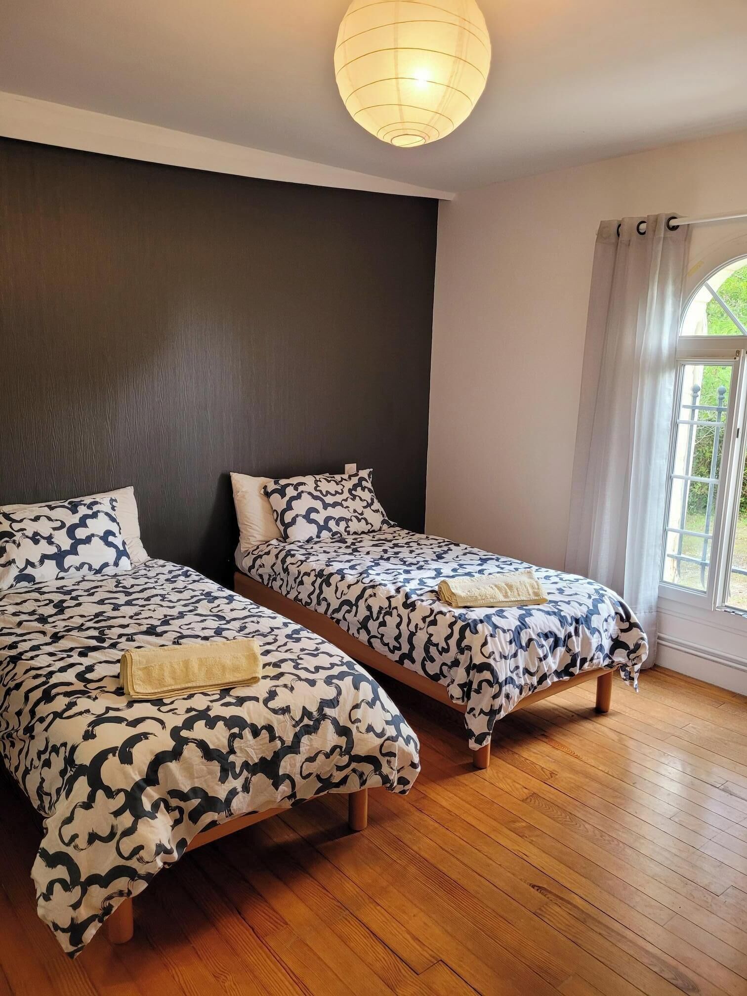Een kamer met twee bedden, een donkere wand, een houten vloer en een raam met gordijnen.