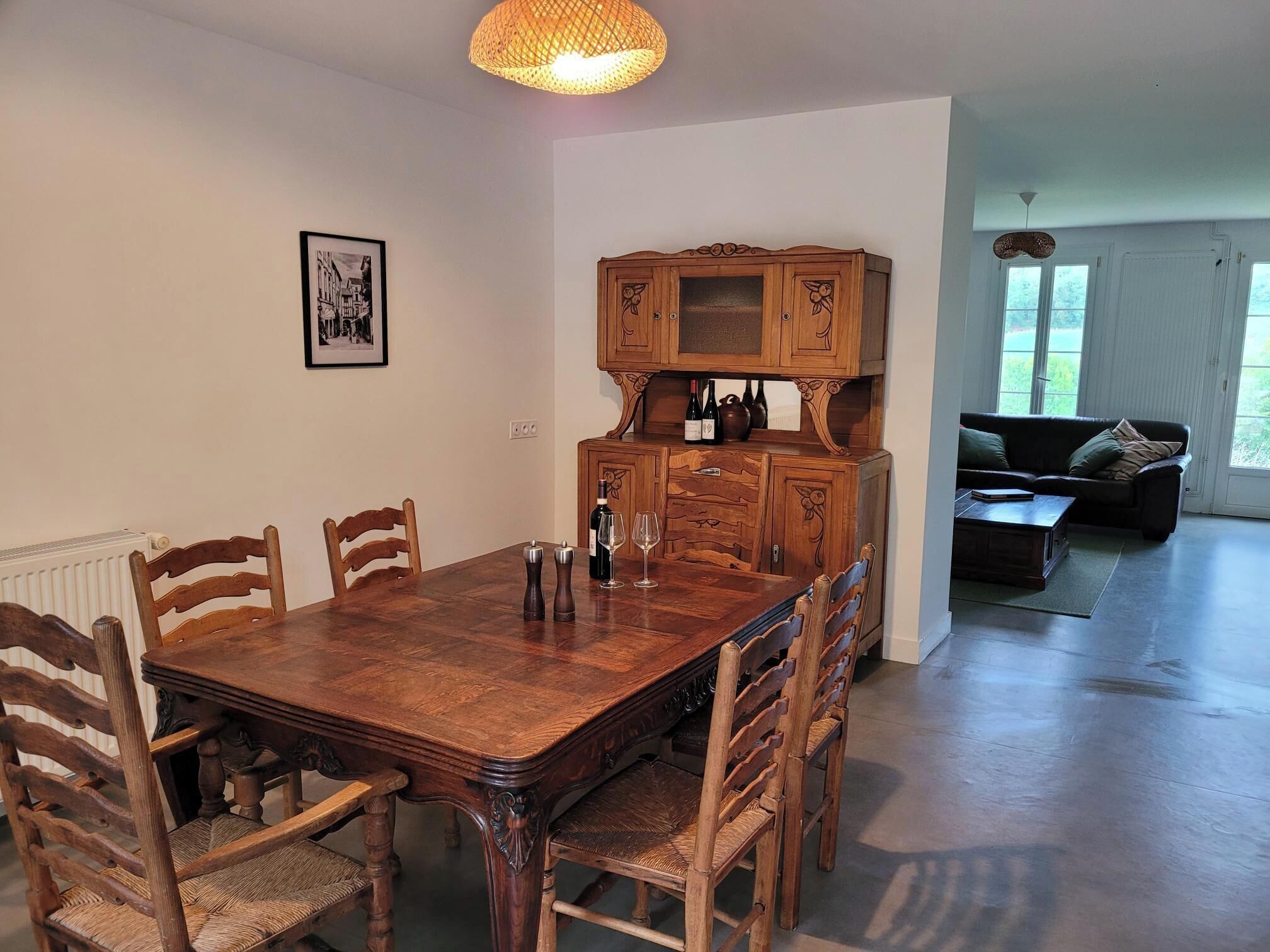 Un comedor con una mesa y sillas de madera, un armario con botellas de vino y un cuadro en la pared.