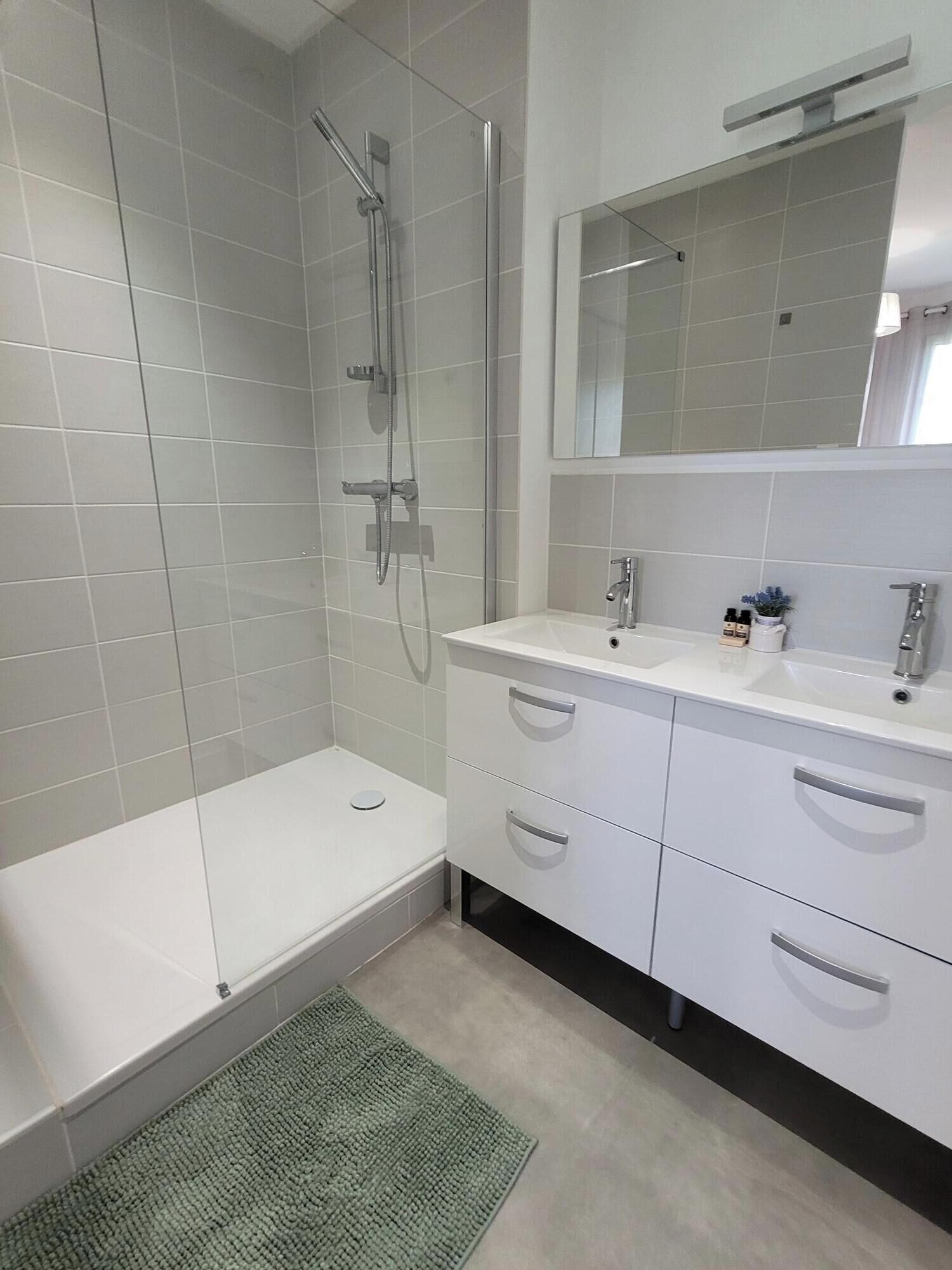 A modern bathroom with a walk-in shower, a white vanity with a mirror, and a green rug.