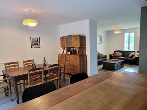 A dining area with a wooden table and chairs, a cabinet with wine bottles, and a living room with a sofa and a coffee table.