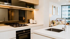 A modern kitchen with a gas stove, white countertops, a built-in oven, and a stainless steel sink. - The Elysian on Margaret at Queen's Wharf (Brisbane City)