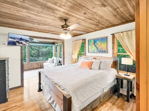 A bedroom with a large bed, a ceiling fan, a television, and a window with a view of trees. - Mountain Melody - Mountain View | Pet Friendly | Hot Tub | Game Room (Morganton)