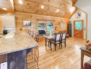 A wooden cabin interior with a dining area, kitchen, and a large window. - Mountain Melody - Mountain View | Pet Friendly | Hot Tub | Game Room (Morganton)
