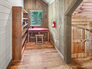 A narrow hallway with wooden walls and a red desk with a stool. A window with a view of trees is visible, and a fire extinguisher is mounted on the wall. - Mountain Melody - Mountain View | Pet Friendly | Hot Tub | Game Room (Morganton)