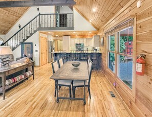 A wooden interior with a dining table, chairs, a kitchen area, and a staircase. - Mountain Melody - Mountain View | Pet Friendly | Hot Tub | Game Room (Morganton)