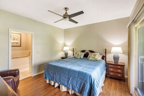 A bedroom with a bed, two bedside tables with lamps, a ceiling fan, and a door leading to a bathroom. - Tall Ship 337 Keowee Key (Salem)