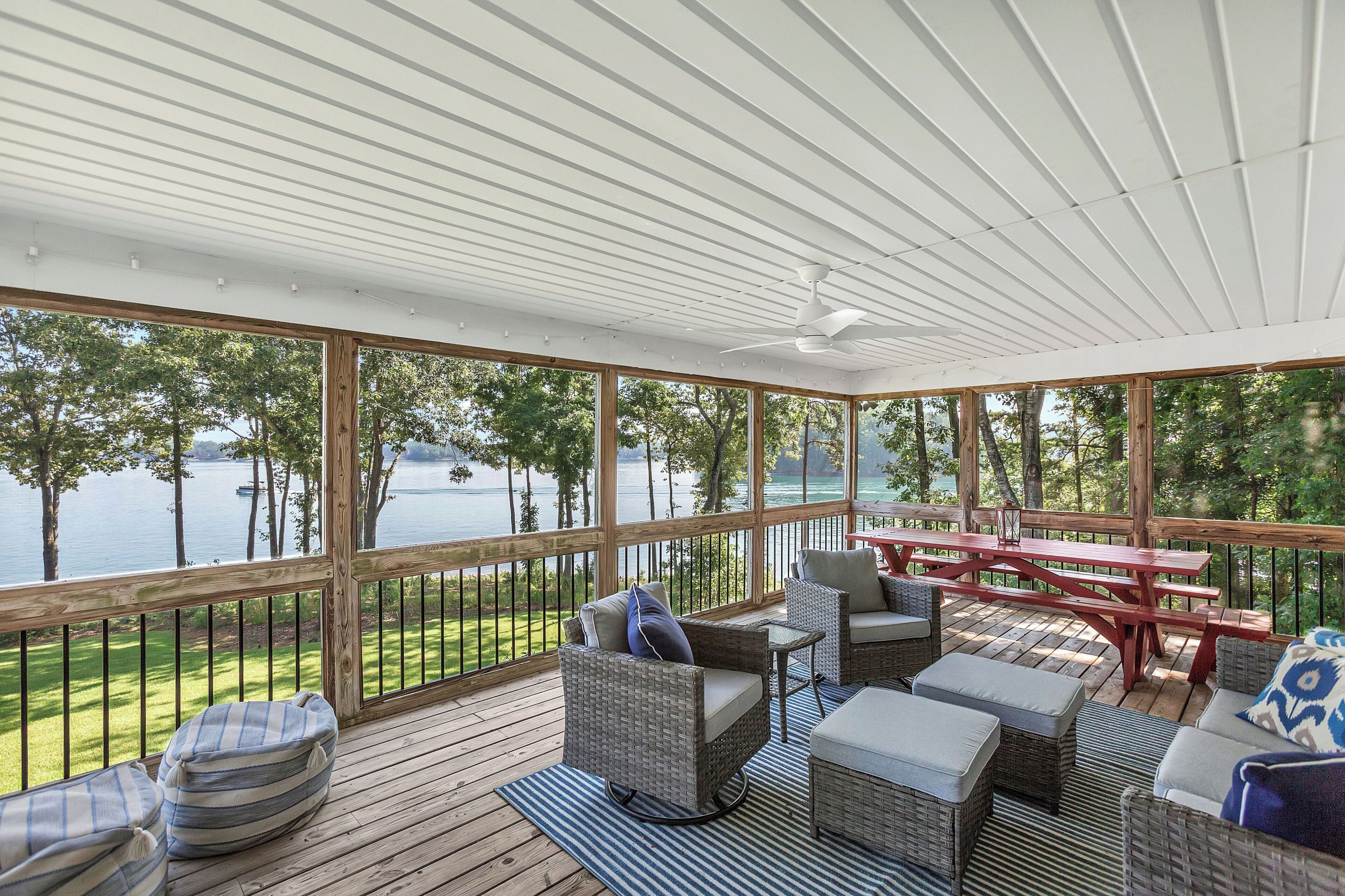 Una terraza techada con mobiliario exterior, una mesa y vista a un lago.