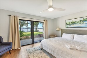 A bedroom with a large bed, a ceiling fan, a nightstand, a lamp, and a painting. - Eagles Point Waterfront Oasis (Seneca)