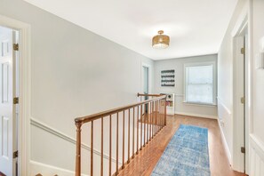 A hallway with a wooden staircase, a blue rug, and a ceiling light fixture. - Eagles Point Waterfront Oasis (Seneca)