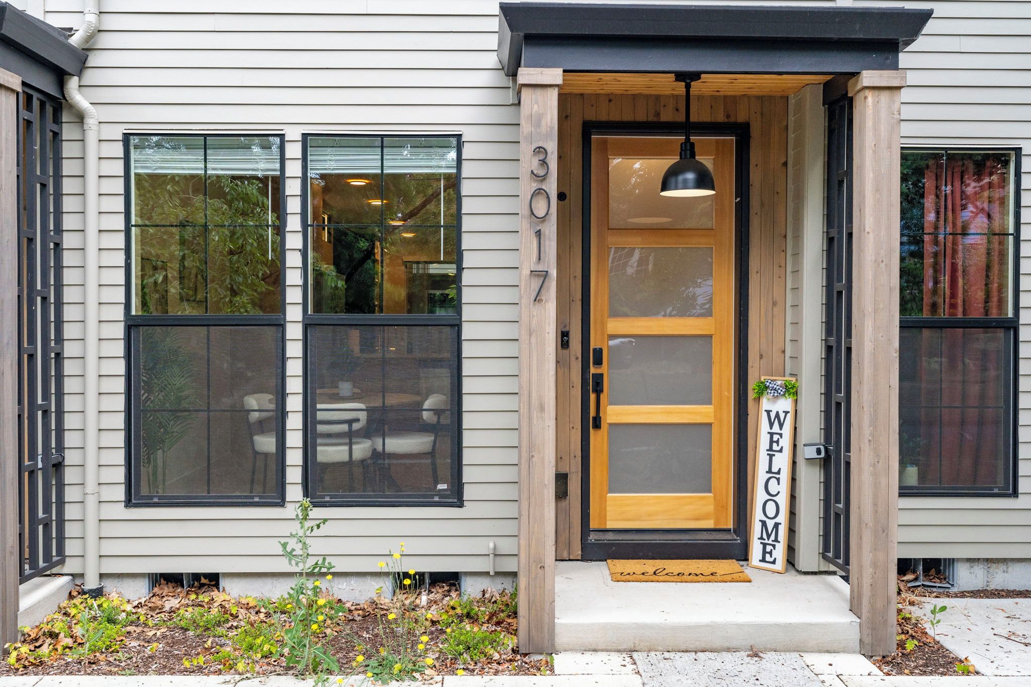 A modern house with a wooden front door, large windows, and a welcome sign.