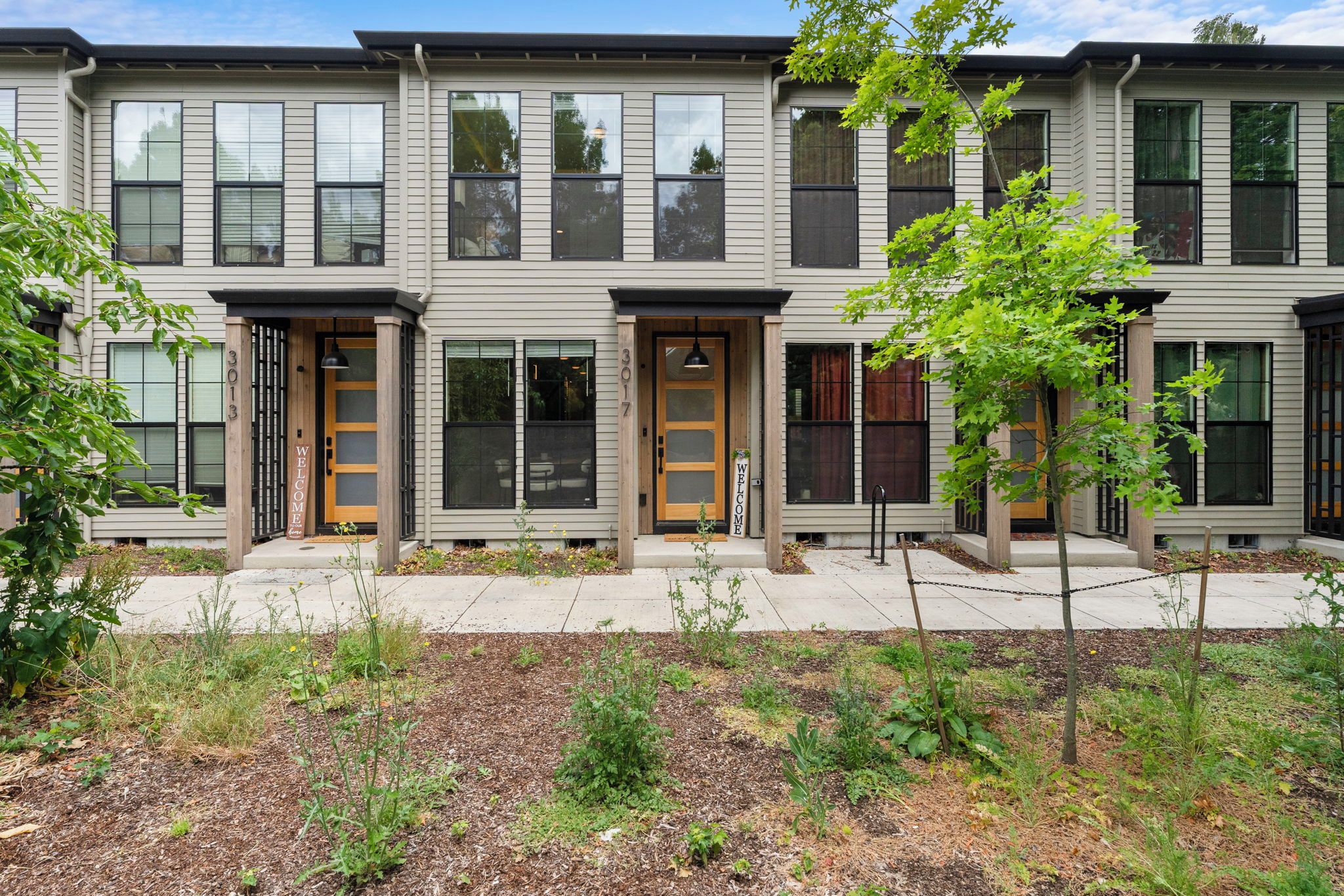 A row of townhouses with a front porch, a welcome sign, and a chain-link fence.