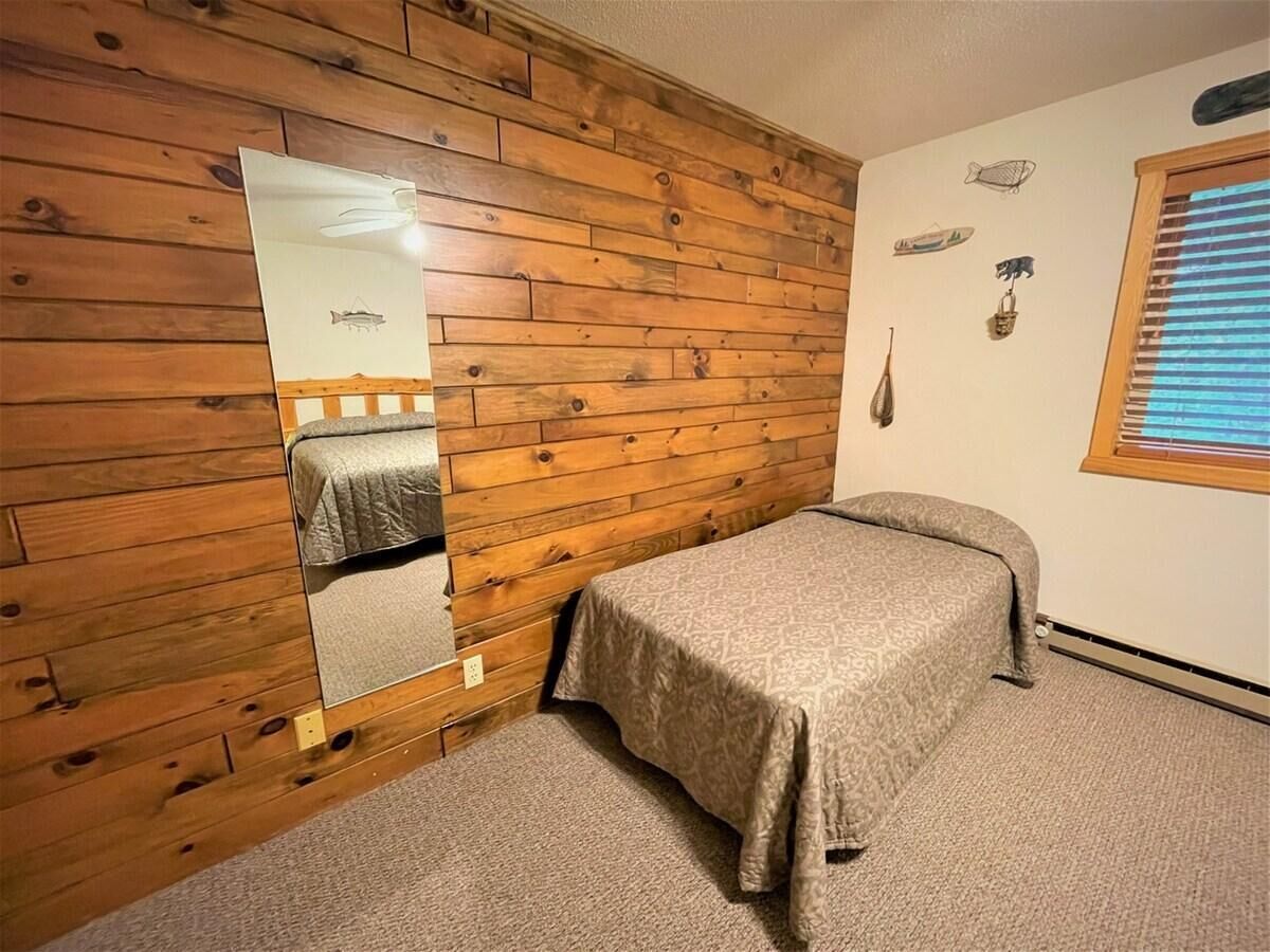 Una cama individual en una habitación con paneles de madera en las paredes y una ventana con persianas.