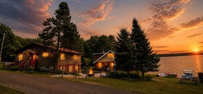 Eine Holzhütte mit Feuerstelle und Steg an einem See bei Sonnenuntergang.