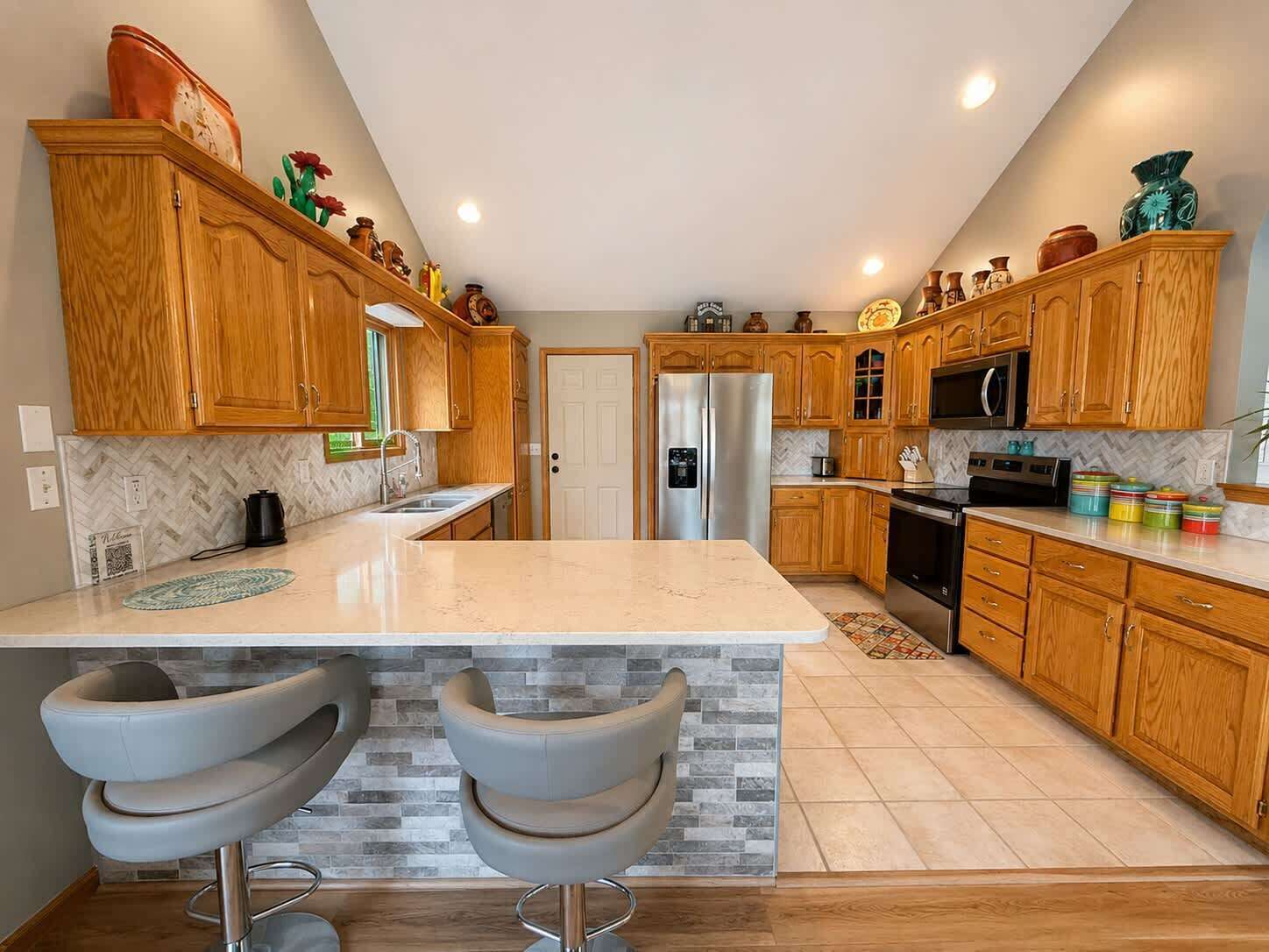 Una cocina moderna con armarios de madera, una isla central, taburetes de bar y un refrigerador.