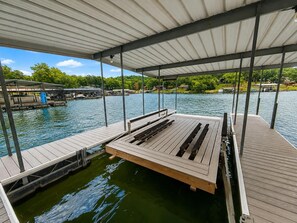 Une jetée abritée, dotée d’une plateforme en bois et de bancs, qui offre une vue sur une étendue d’eau calme, avec un bateau amarré et des bâtiments en arrière-plan.