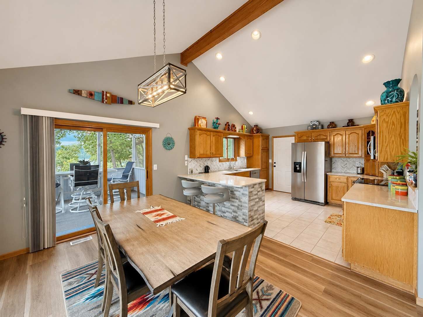 A modern kitchen with wooden cabinets, a stainless steel refrigerator, and a dining area with a wooden table and chairs.