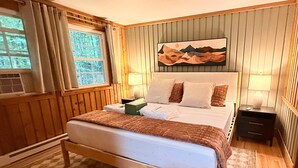 A bedroom with a wooden bed, a nightstand, a lamp, and a painting on the wall. - Firelight Escape w/ Hot Tub, Games & Resort Access (Tobyhanna Township)