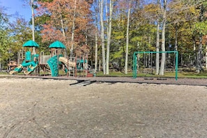 Ein Spielplatz mit Klettergerüsten und einer Schaukel in einem von Bäumen gesäumten Park.