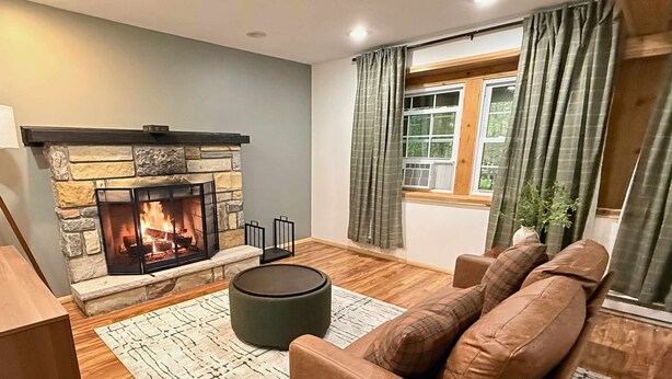 A living room with a stone fireplace, a brown leather sofa, and a patterned rug. - Firelight Escape w/ Hot Tub, Games & Resort Access (Tobyhanna Township)