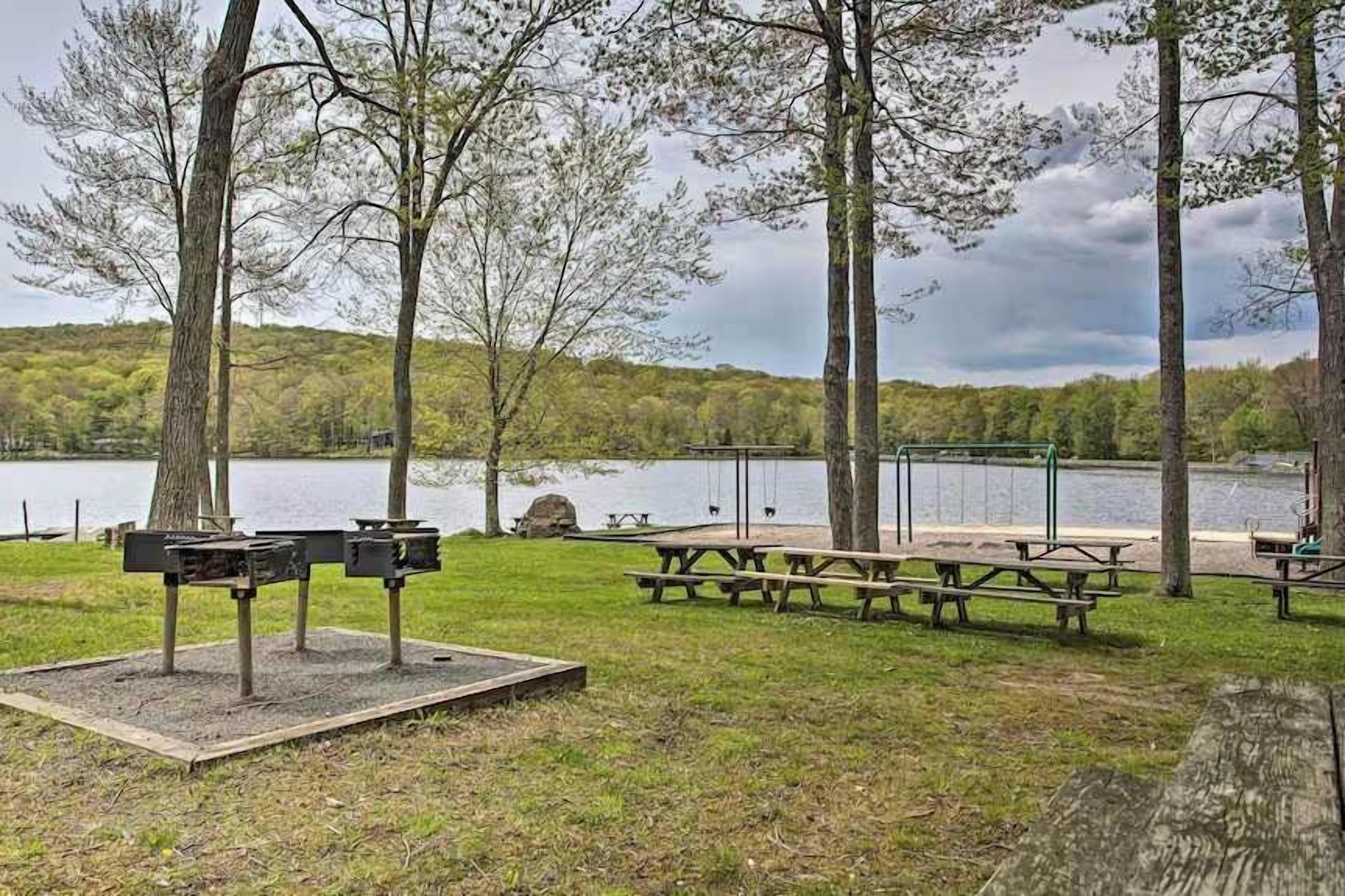 A lakeside park with picnic tables and benches, surrounded by trees and a view of the lake.
