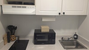 A kitchen with white cabinets, a black microwave, a stainless steel sink, and a dishwasher. - Modern & Cozy Studio in Midtown (Atlanta)