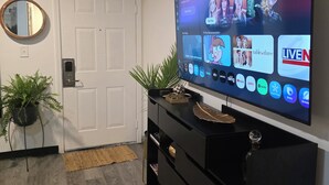 A modern living room with a flat-screen TV mounted on the wall, a black entertainment unit below, a round mirror, and a potted plant. - Modern & Cozy Studio in Midtown (Atlanta)