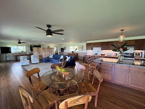 A spacious living area with a glass dining table surrounded by wooden chairs, a blue sectional sofa, and a ceiling fan.