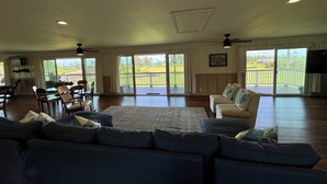 A spacious living room with a large sofa, a dining area, and a balcony with a view. - Tranquil 1-bedroom cottage across from the beach perfect for North Shore getaway (Kahuku)