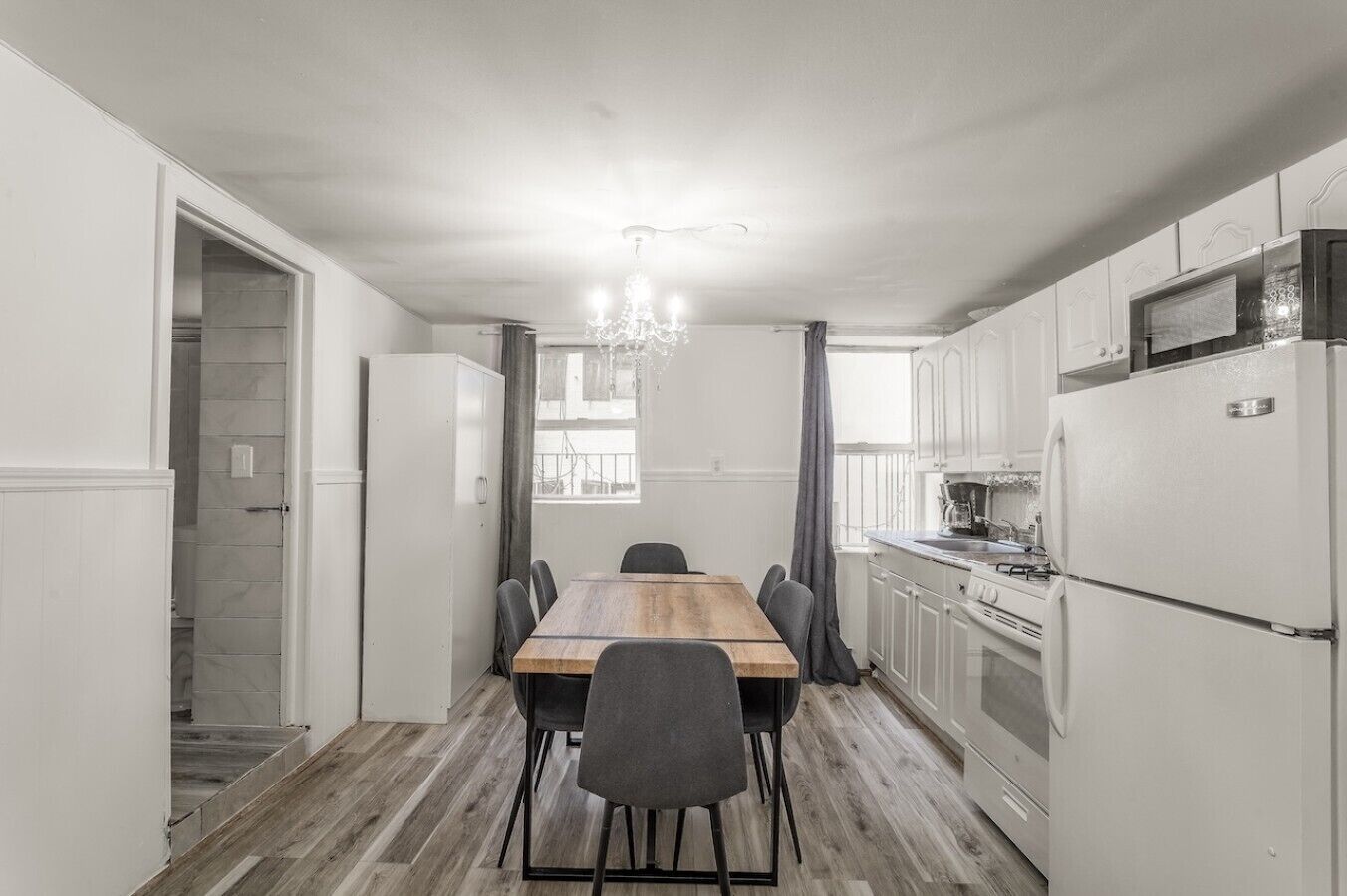 A modern kitchen with white cabinetry, a wooden dining table, and a chandelier.