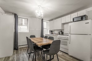 A compact kitchen with a dining table, chairs, a chandelier, and a refrigerator.
