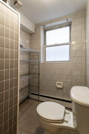A bathroom with a toilet, a window, and metal shelving units.