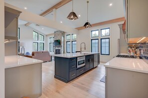 A spacious kitchen with a central island, large windows, and a stone fireplace.