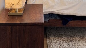 Un dormitorio con una cama, almohadas, una mesita de noche y una lámpara.