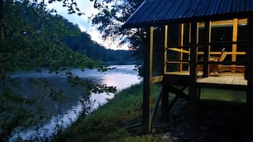 A wooden cabin with a deck overlooking a calm lake, surrounded by trees.