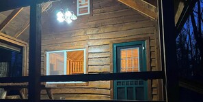Une cabane en bois avec une fenêtre et une porte apparentes, un espace intérieur visible et un plafond apparent.