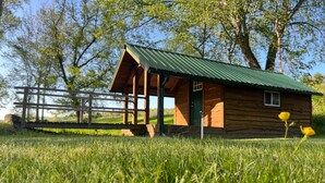 A wooden cabin with a green roof, surrounded by a wooden fence and lush green grass.