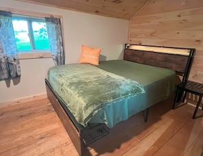 Una cama individual con cabecera, una ventana con cortinas y suelo de madera.