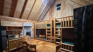 A wooden cabin interior with a dining table, chairs, a kitchen area, and bunk beds. - :)Over The River Through The Woods Comfy4Q Beds #4 (Belfast)