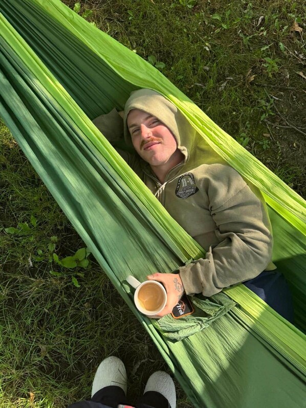Una persona recostada en una hamaca al aire libre, rodeada de hierba y plantas.