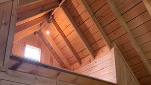 A wooden interior with a sloped ceiling, a window with a view of greenery, and a light fixture. - :)Over The River Through The Woods Comfy4Q Beds #4 (Belfast)
