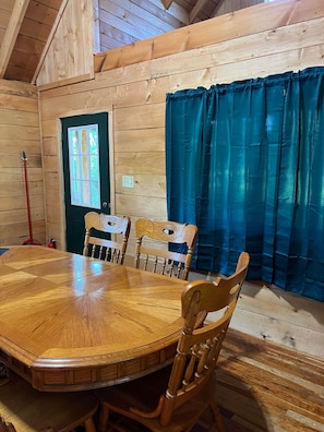 Un intérieur en bois avec une table de salle à manger ronde, des chaises, une fenêtre et des rideaux.