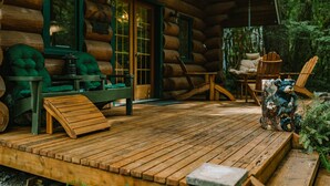 Eine Blockhütte mit einer Holzterrasse, grünen Sitzgelegenheiten mit Polstern und einer rustikalen Bärenskulptur.