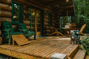 Eine Blockhütte mit einer Holzterrasse, grünen Sitzgelegenheiten mit Polstern und einer rustikalen Bärenskulptur.