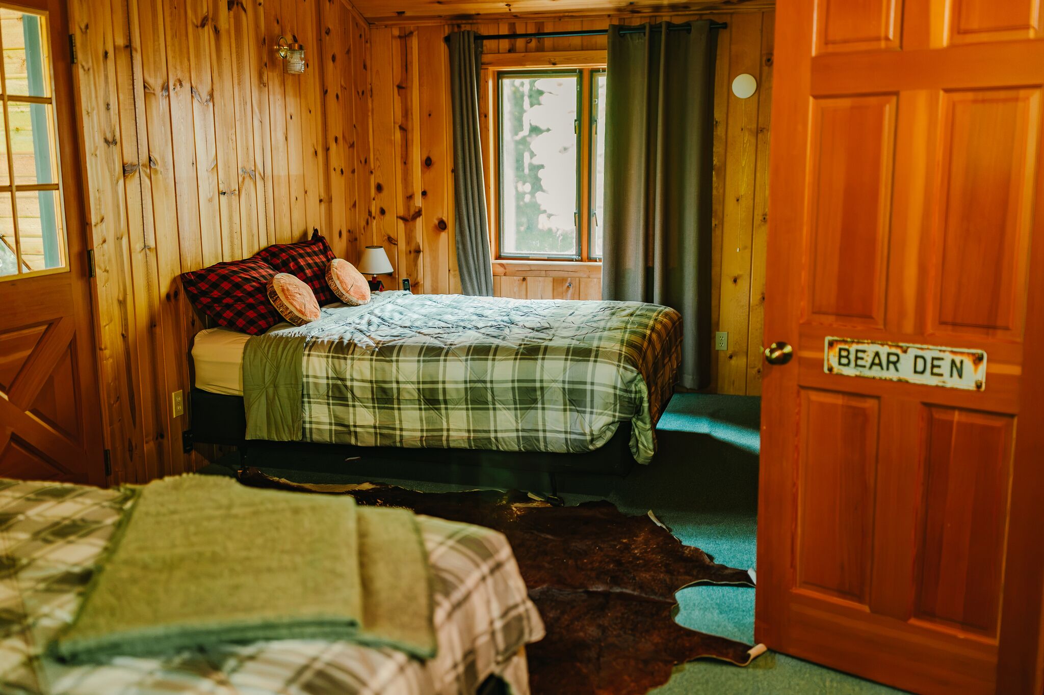 A cabin interior with a bed, a wooden door with a sign, and a window with curtains.